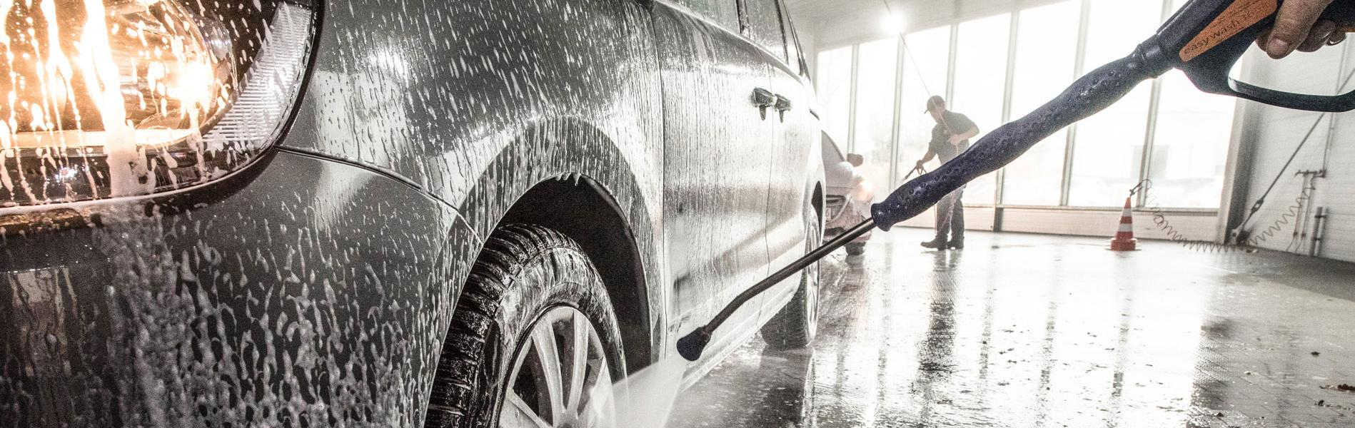 Mitarbeiter wäscht Auto in Waschstraße mit Hochdruckreiniger