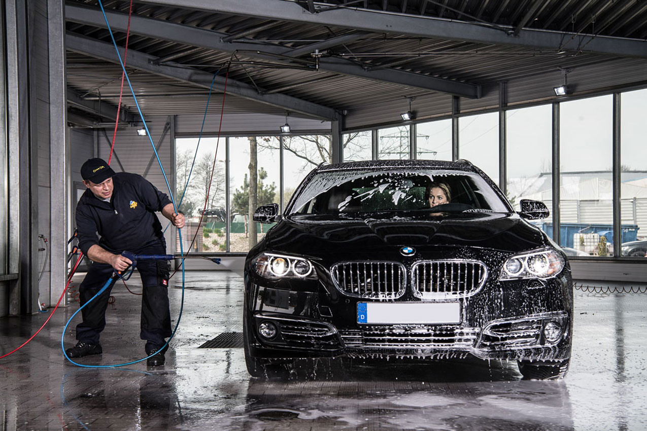 Mitarbeiter wäscht Auto in Waschstraße mit Hochdruckreiniger