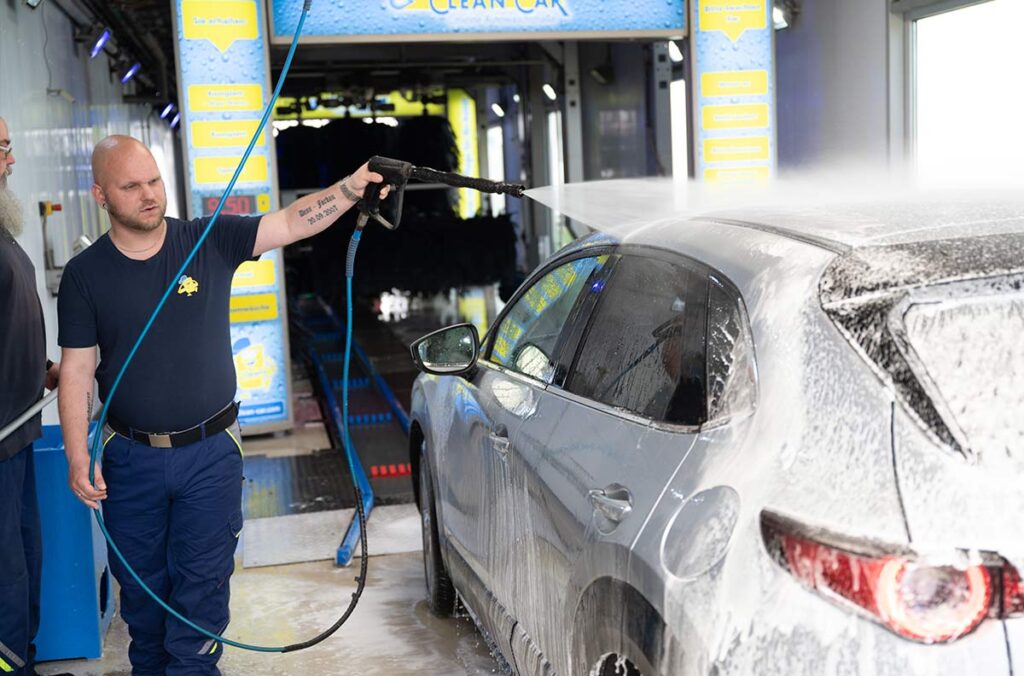 Mitarbeiter wäscht Auto in Waschstraße mit Hochdruckreiniger